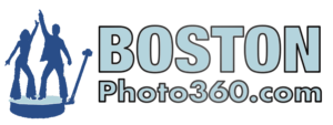 The image features the logo for “BostonPhoto360.com.” The design includes two silhouetted figures, a man and a woman, standing on a circular platform, possibly representing the 360 photo booth experience. The man is holding what appears to be a camera or selfie stick, and both figures have their arms raised, suggesting celebration or fun. The text “BOSTON” is in large, light blue uppercase letters, and “Photo360.com” is written below in a smaller font, emphasizing the business name and web address.